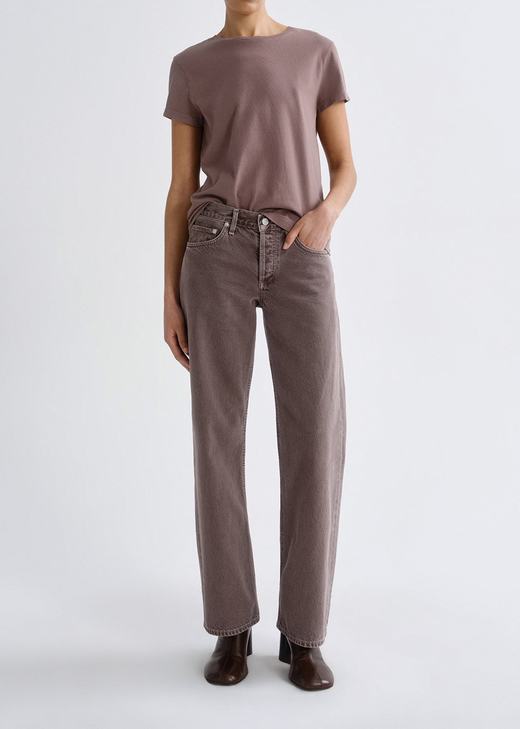 Person wearing a mauve short sleeve crewneck tee with mauve straight leg jeans on a grey background