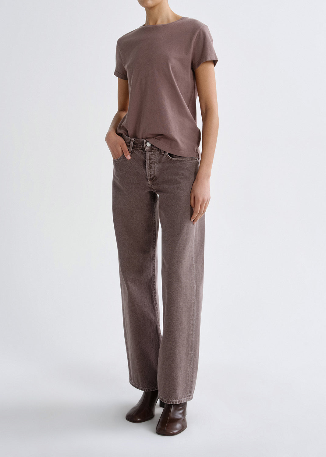 Person wearing a mauve short sleeve crewneck tee with mauve straight leg jeans on a grey background