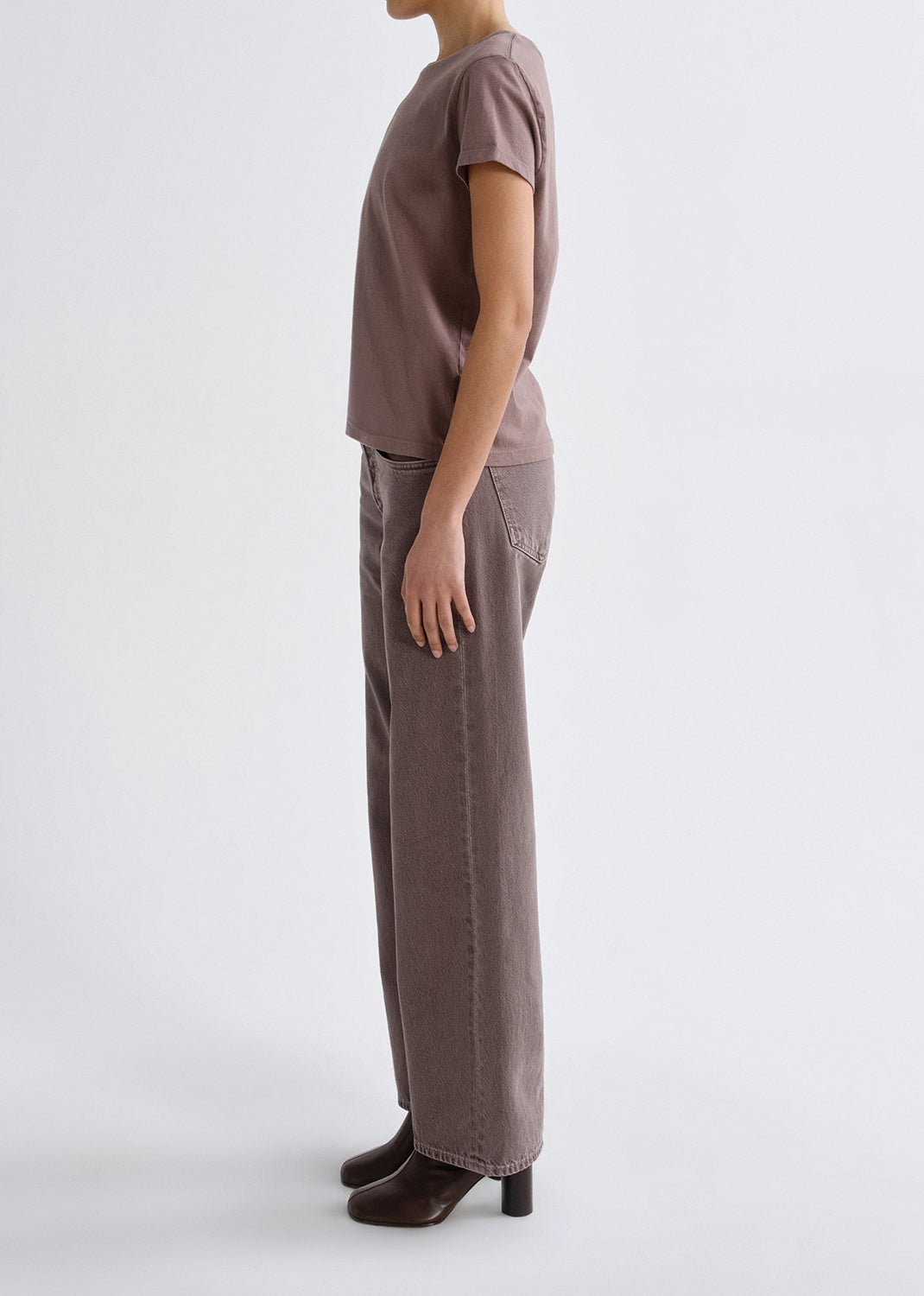 Person wearing a mauve short sleeve crewneck tee with mauve straight leg jeans viewed from the side on a grey background