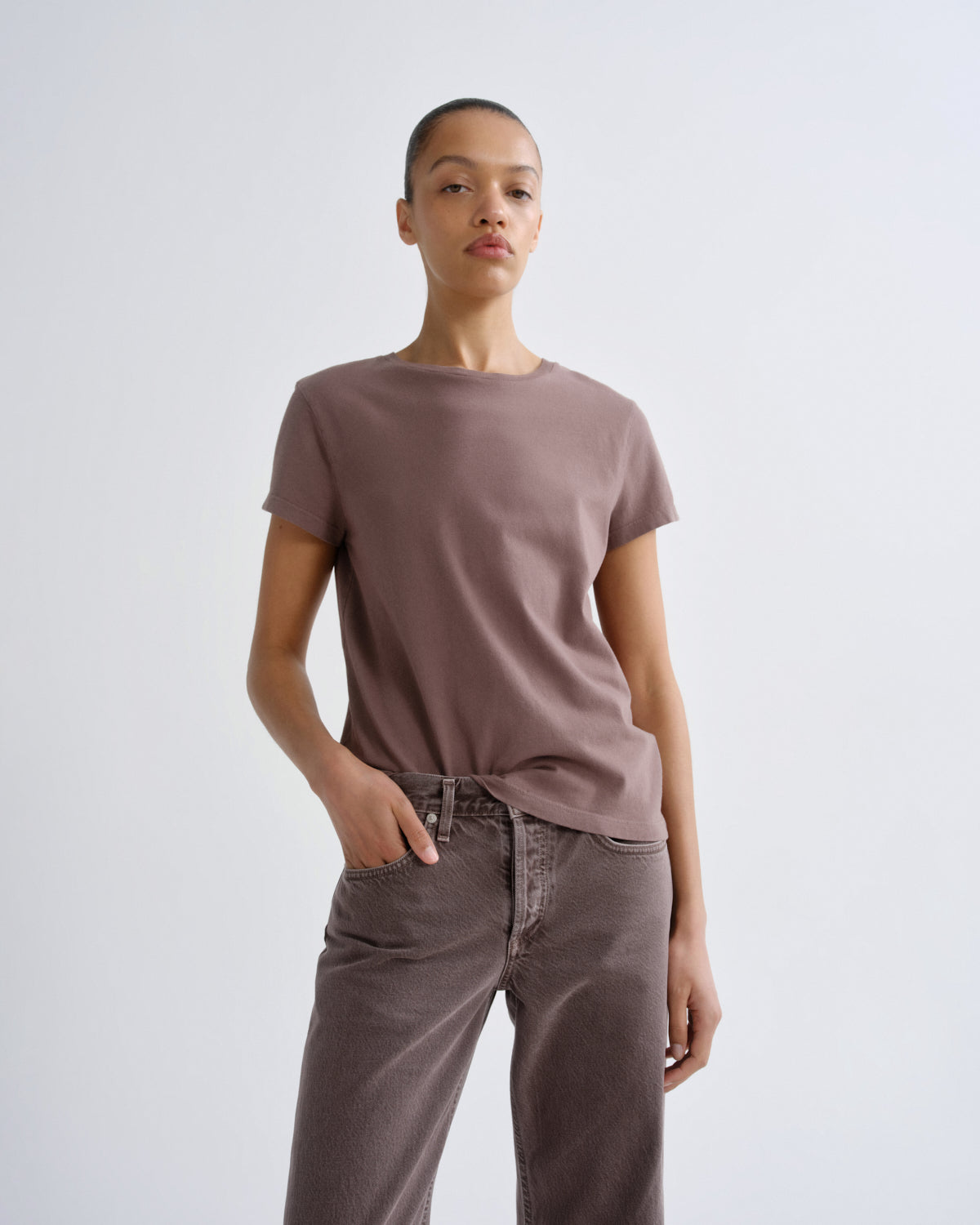 Person wearing a brown t-shirt and pants against a white background
