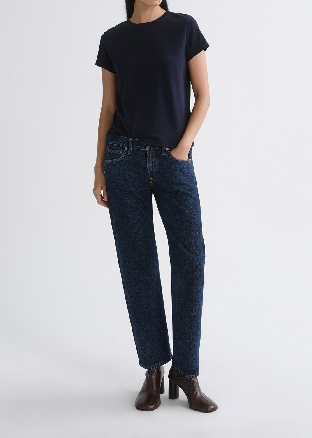Person wearing a black t-shirt and dark blue jeans on a grey background
