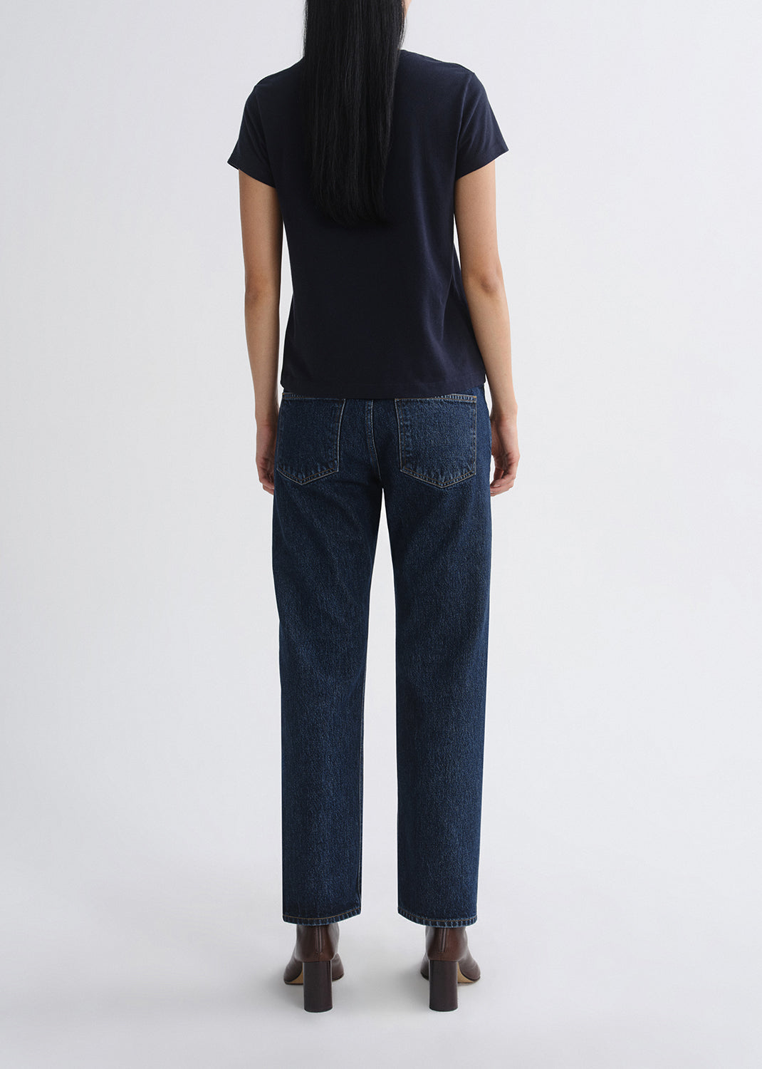 Person wearing a black t-shirt and dark blue jeans on a grey background