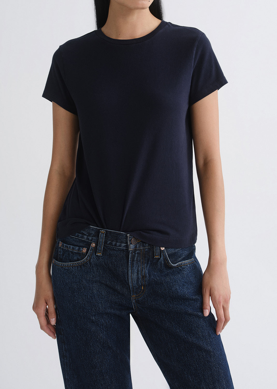 Person wearing a black t-shirt and blue jeans on a grey background
