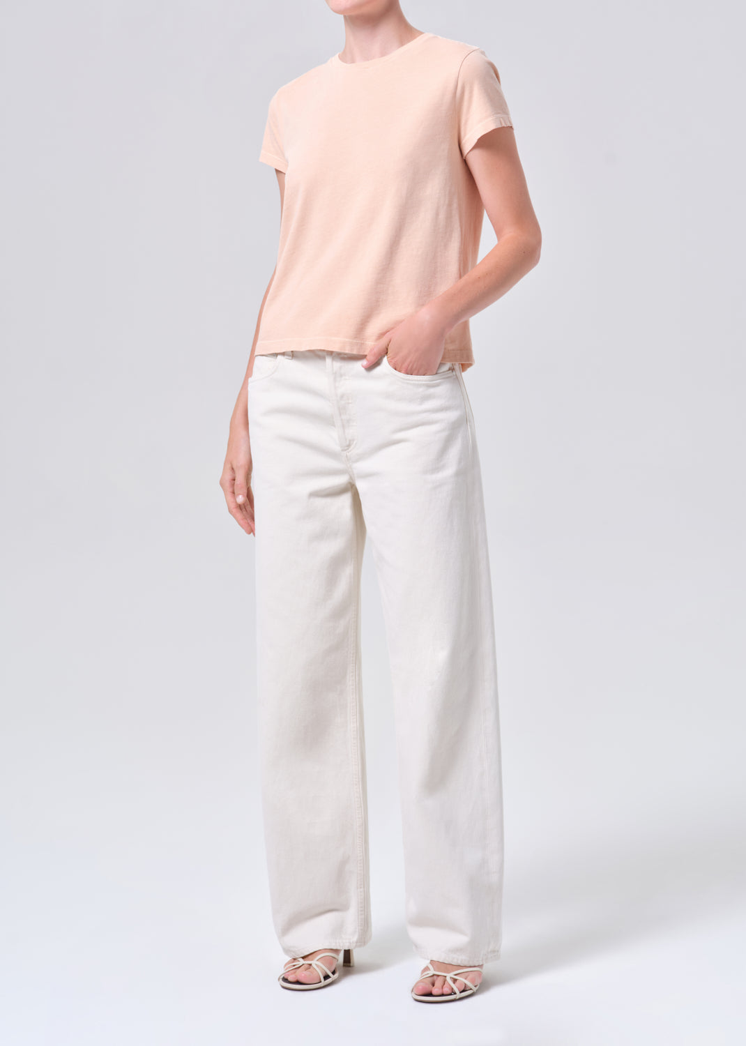Person wearing a light pink t-shirt and white pants on a white background