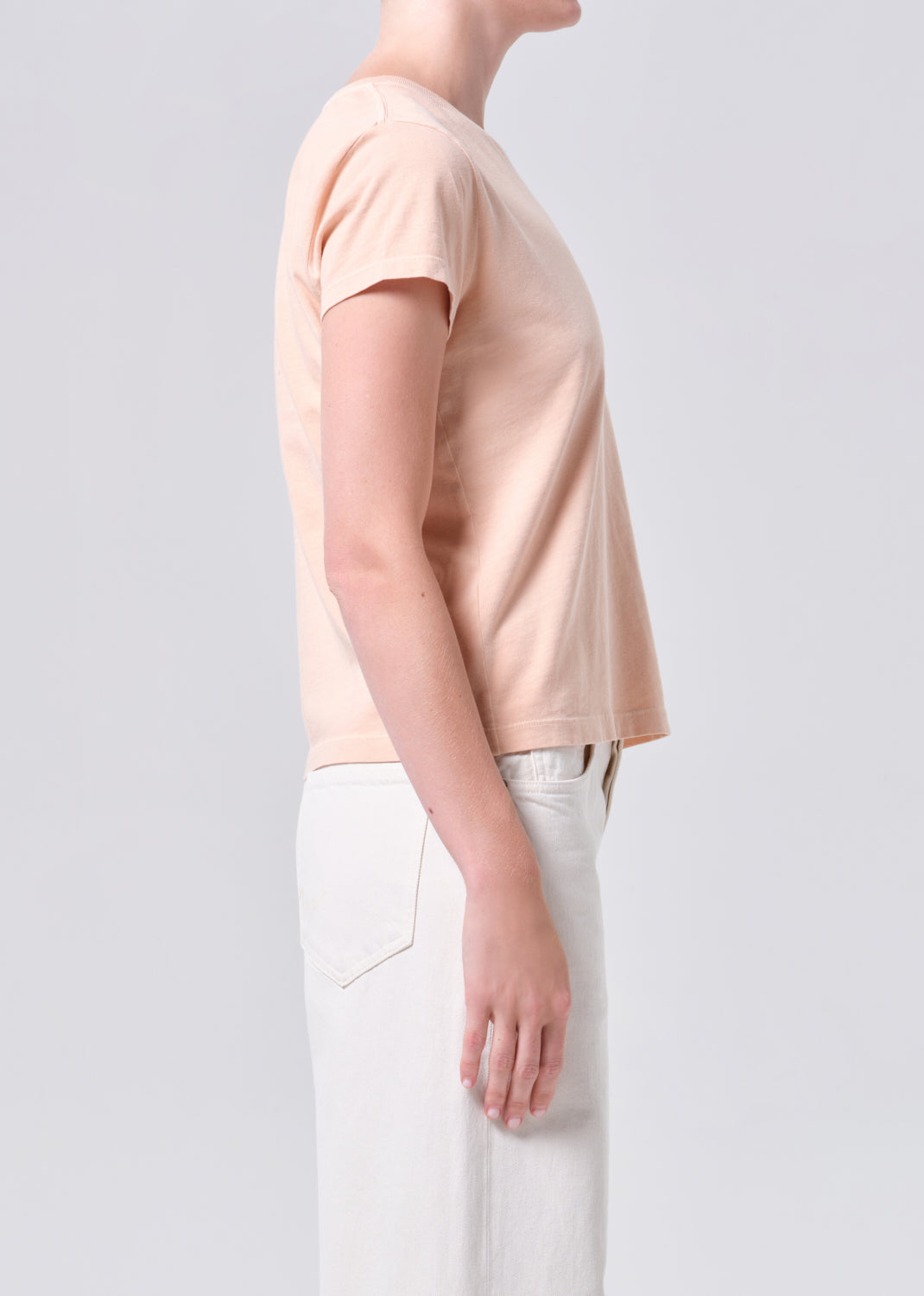 Person wearing a light pink t-shirt and white pants on a plain background