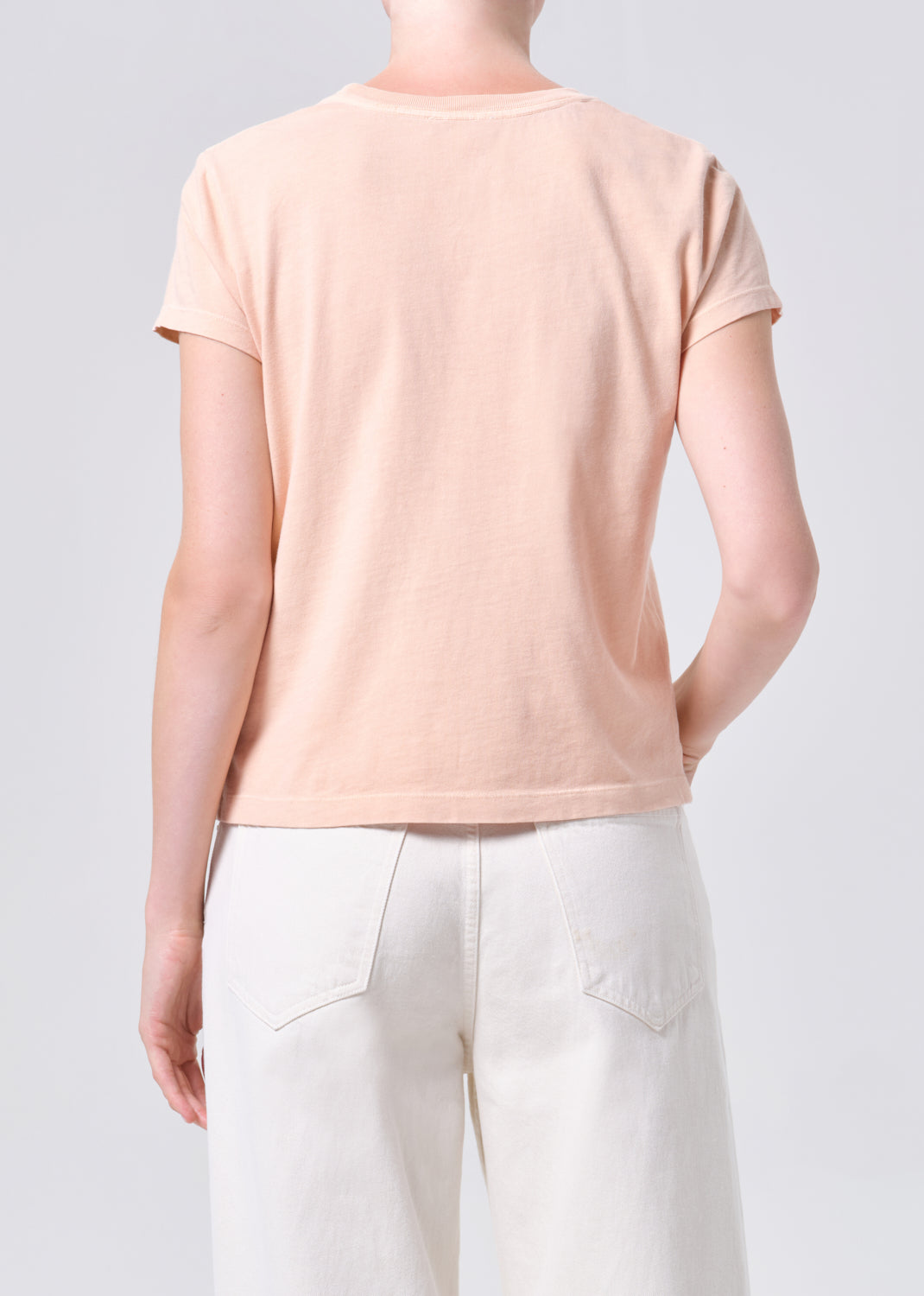 Person wearing a light pink t-shirt and white pants on a plain background