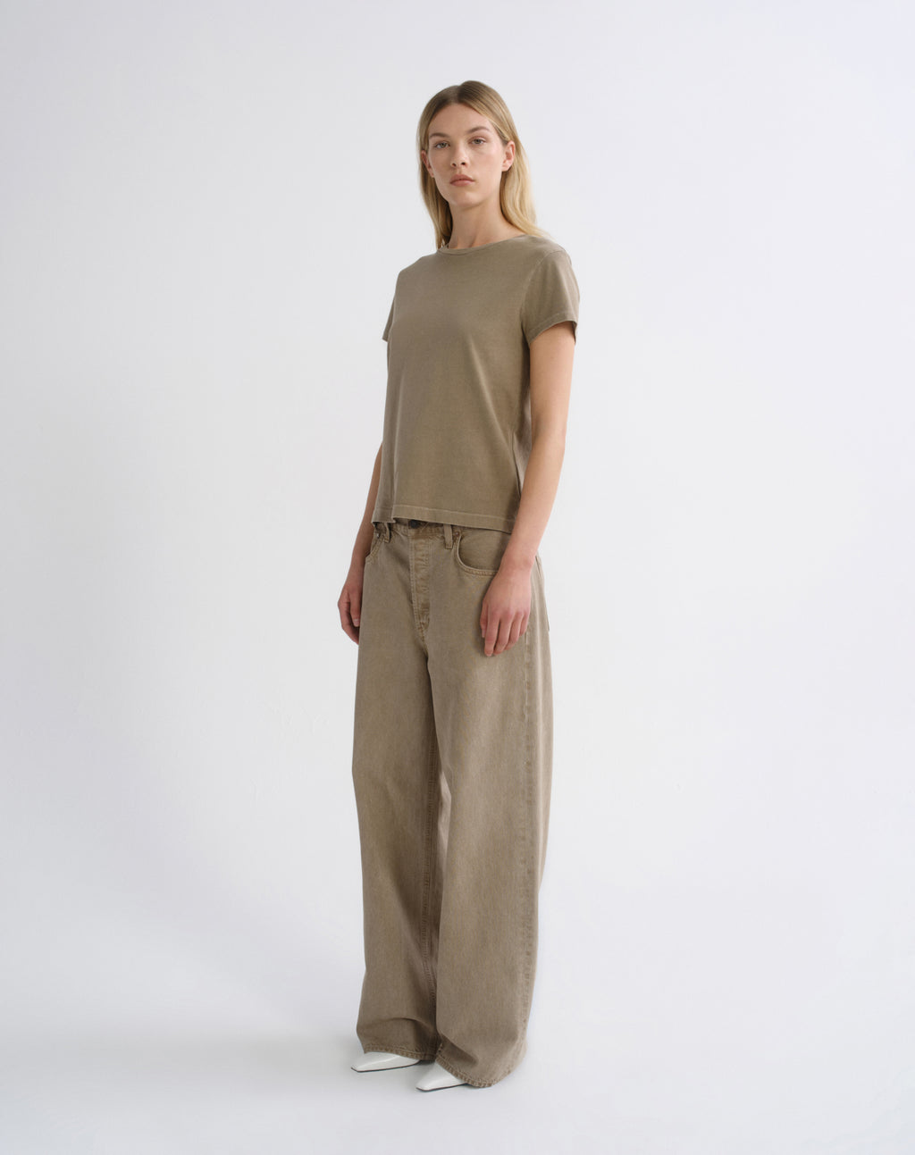 A woman modeling a matching taupe-brown short-sleeve crewneck t-shirt and wide-leg trousers set, standing against a clean white studio background.
