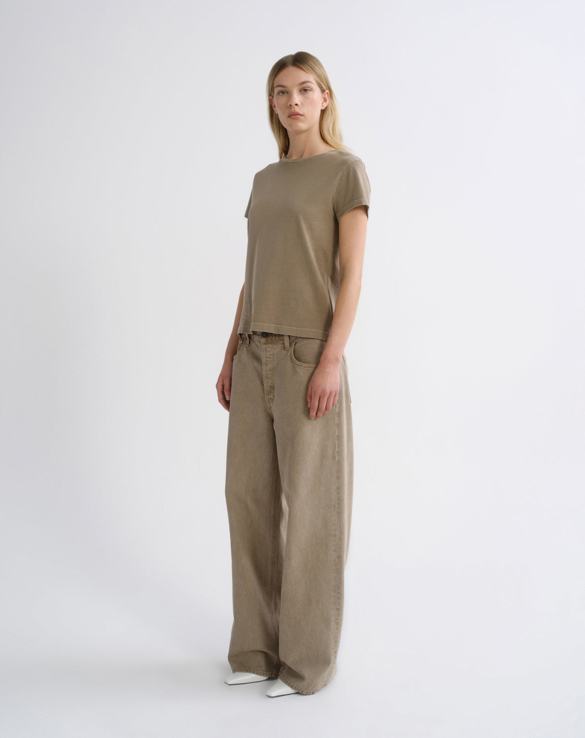A woman modeling a matching taupe-brown short-sleeve crewneck t-shirt and wide-leg trousers set, standing against a clean white studio background.