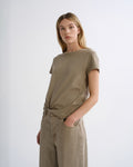 A woman modeling a short-sleeve t-shirt and matching wide-leg trousers in a solid taupe-beige color, standing against a plain light gray studio background.