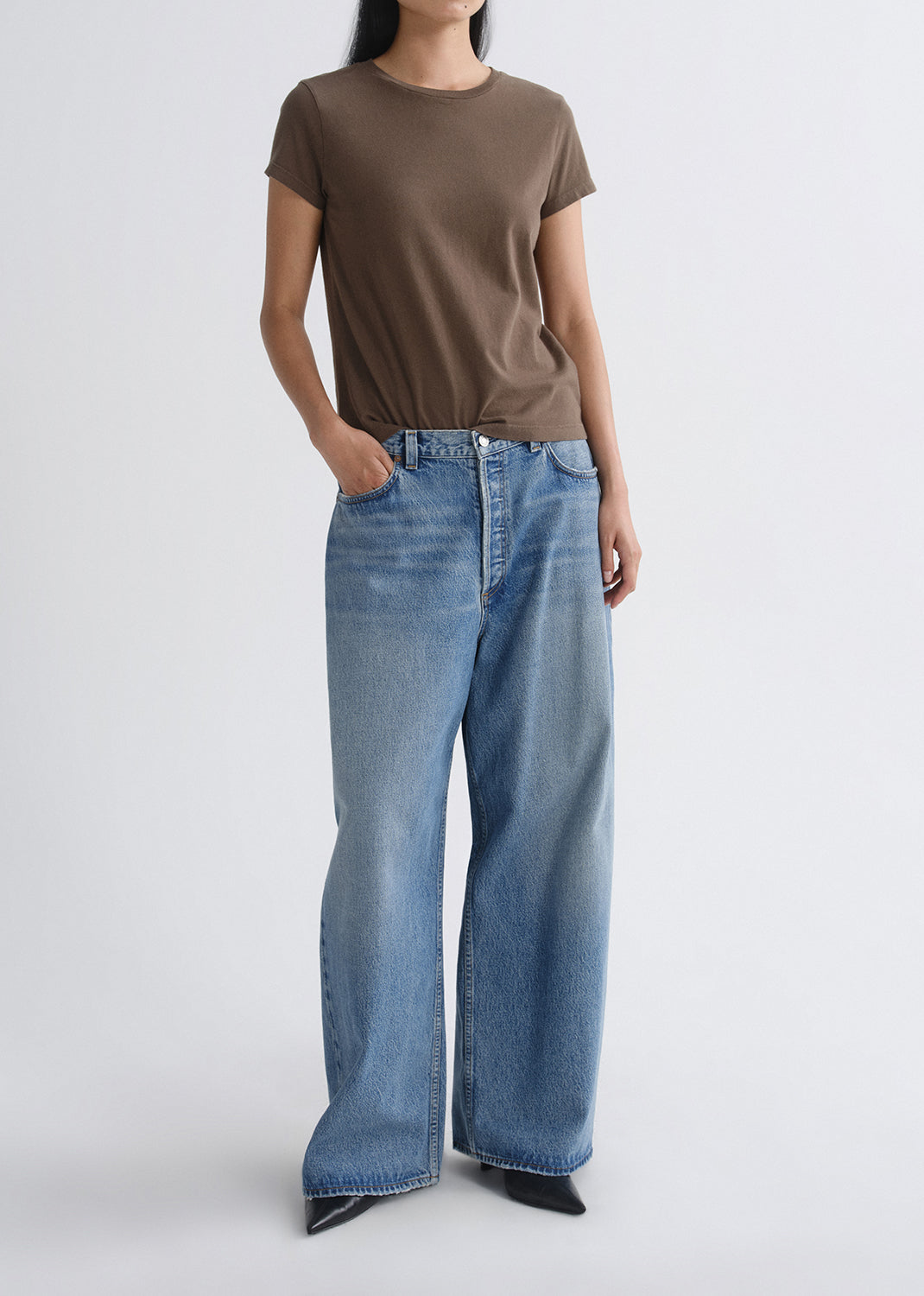 Person wearing a brown short sleeve crewneck tee with light wash wide leg jeans on a grey background
