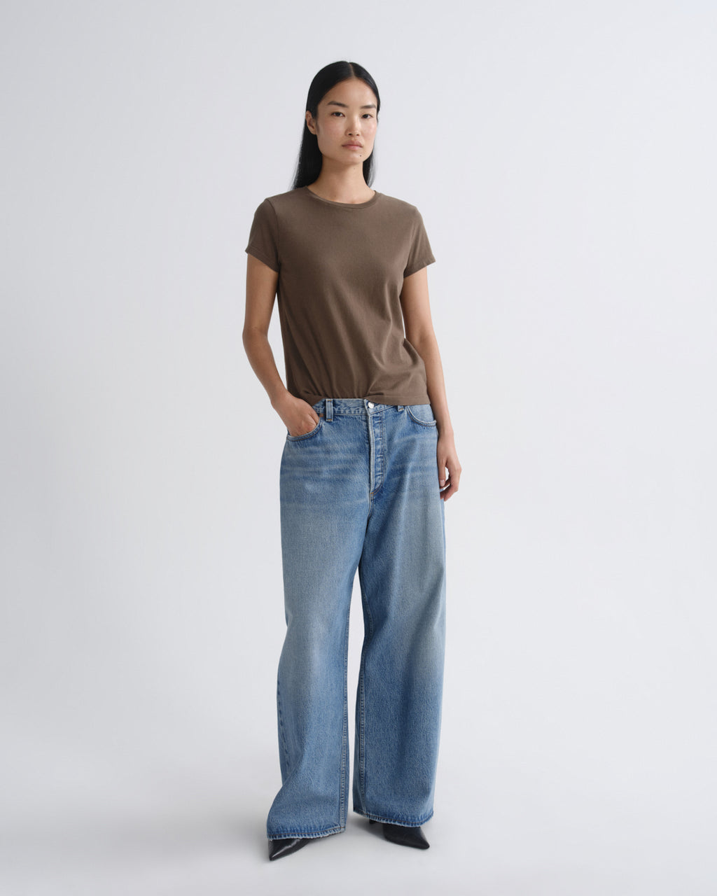 Person wearing a brown t-shirt and blue jeans on a white background