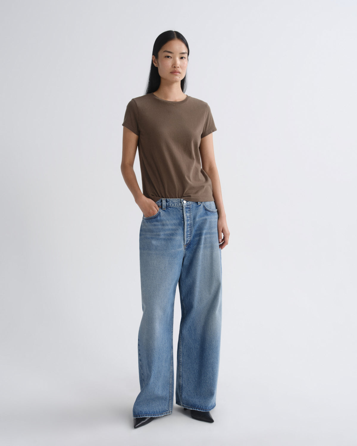 Person wearing a brown t-shirt and blue jeans on a white background