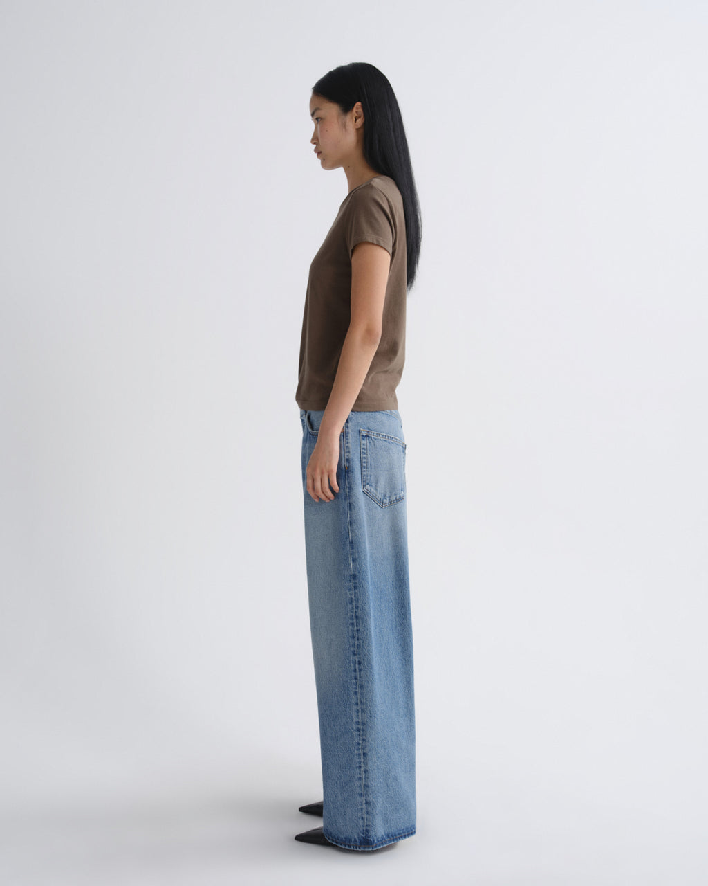 Person wearing a brown top and blue jeans standing against a white background