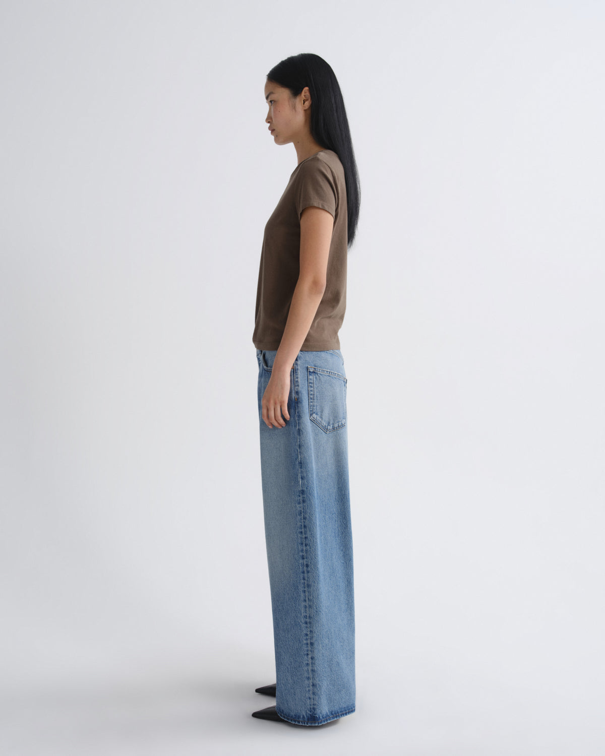 Person wearing a brown top and blue jeans standing against a white background