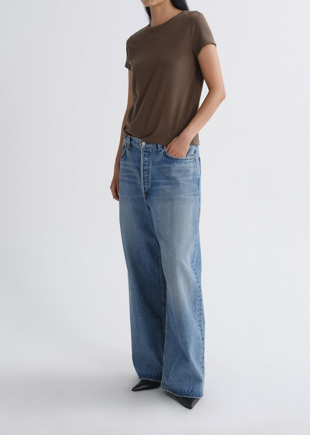 Person wearing a brown short sleeve crewneck tee with light wash wide leg jeans on a grey background