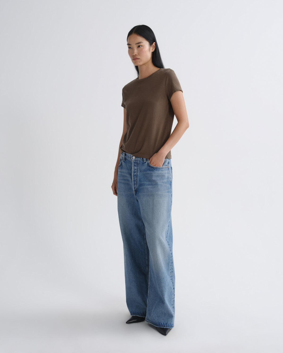 Woman wearing a brown t-shirt and blue jeans on a white background