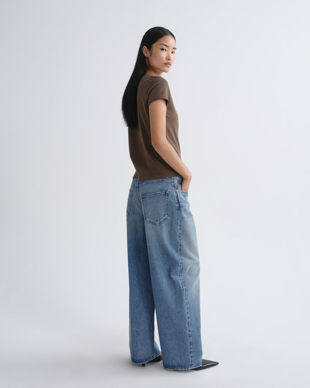Person wearing a brown shirt and blue jeans on a white background
