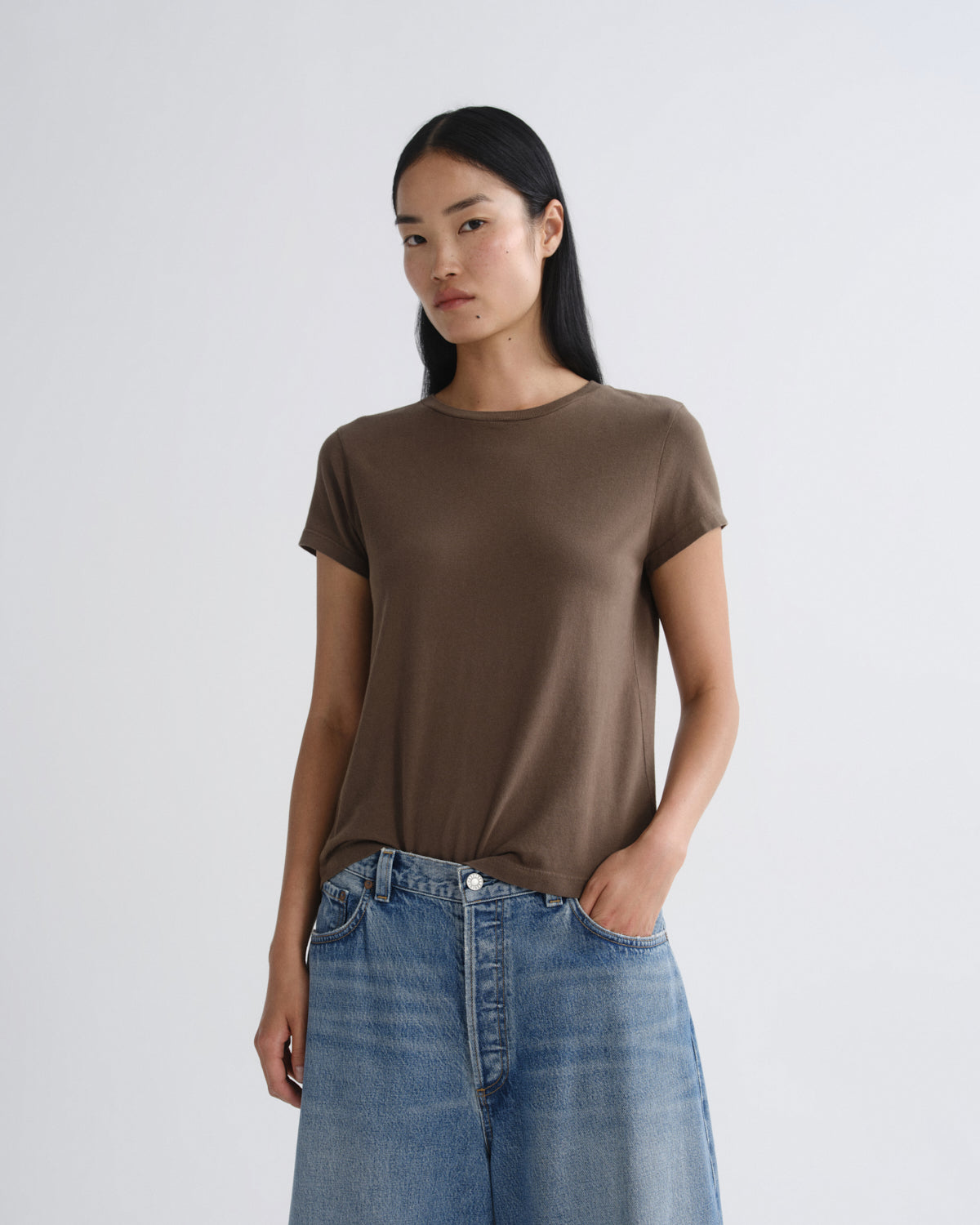 Woman wearing a brown t-shirt and blue jeans against a white background