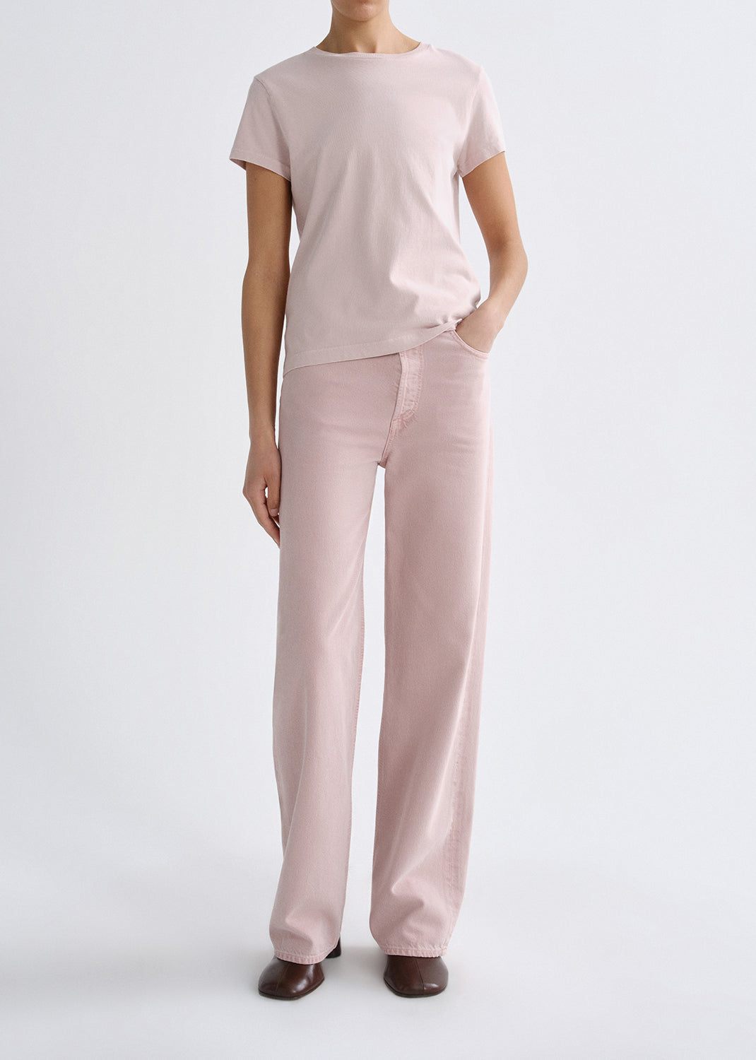 Person wearing a light pink short sleeve crewneck tee with light pink straight leg jeans on a grey background