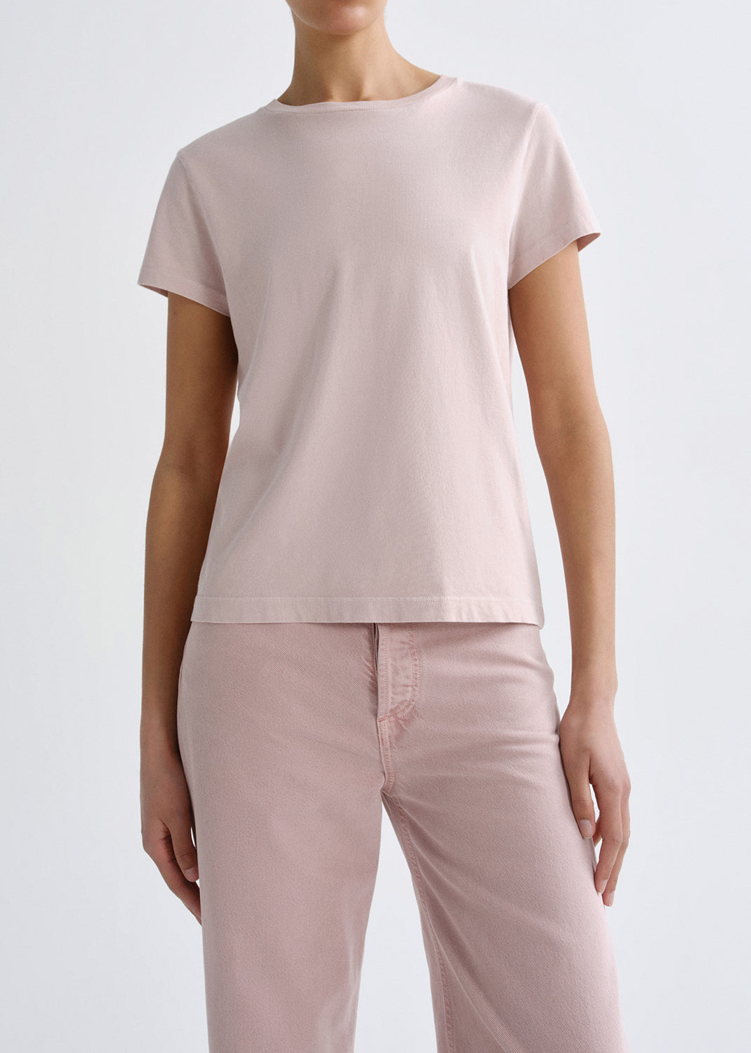 Person wearing a light pink short sleeve crewneck tee with light pink straight leg jeans on a grey background