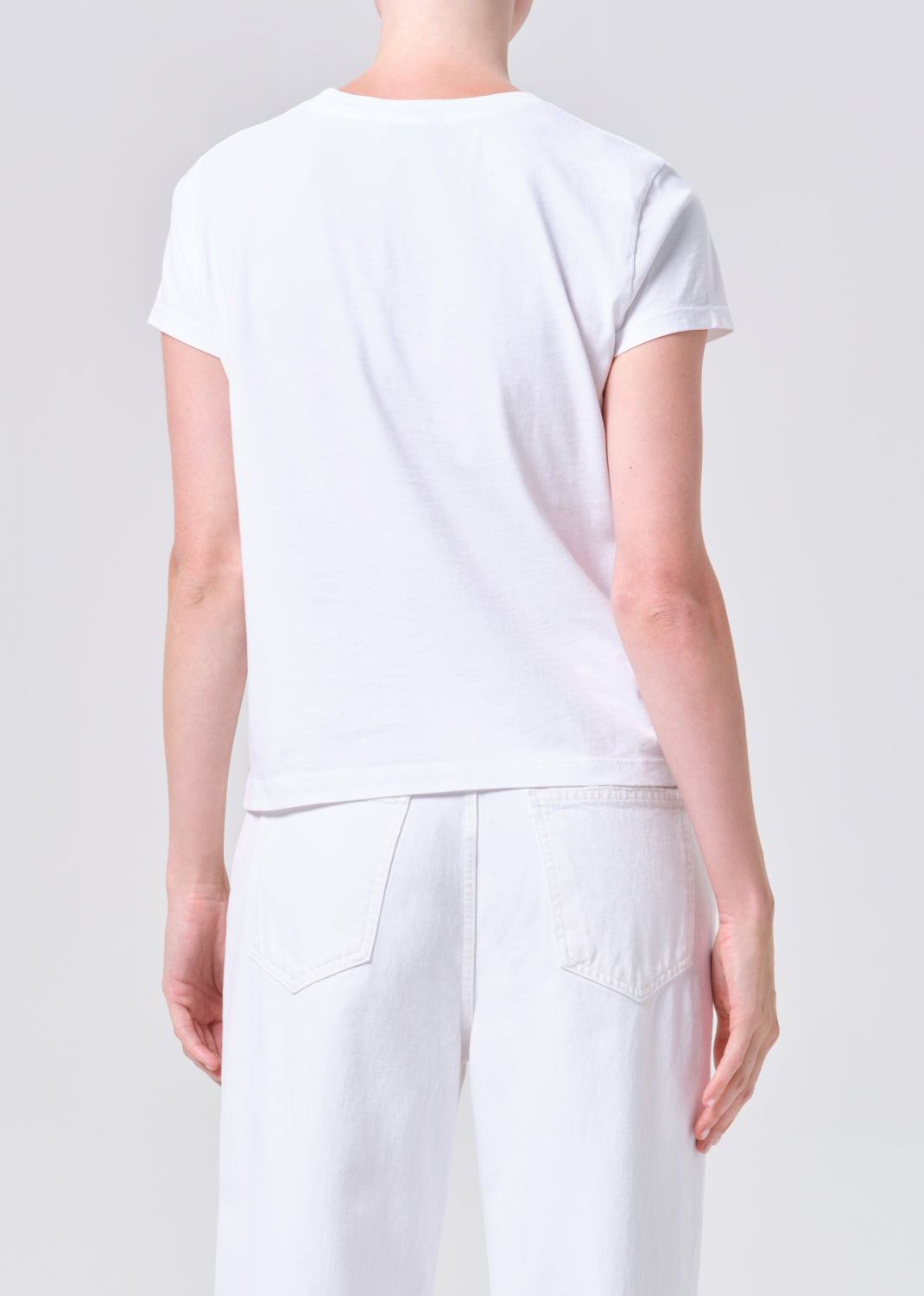 Person wearing a plain white t-shirt and pants on a light gray background