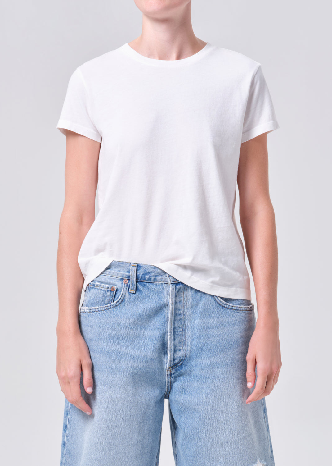 Person wearing a white t-shirt and light blue jeans on a plain background