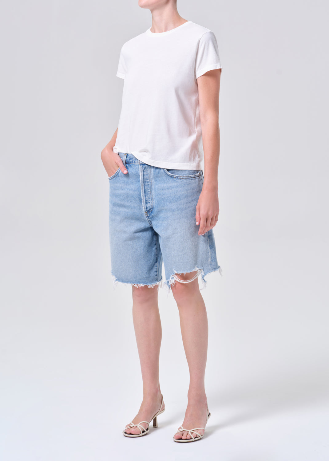 Person wearing a white t-shirt and light blue denim shorts on a plain background