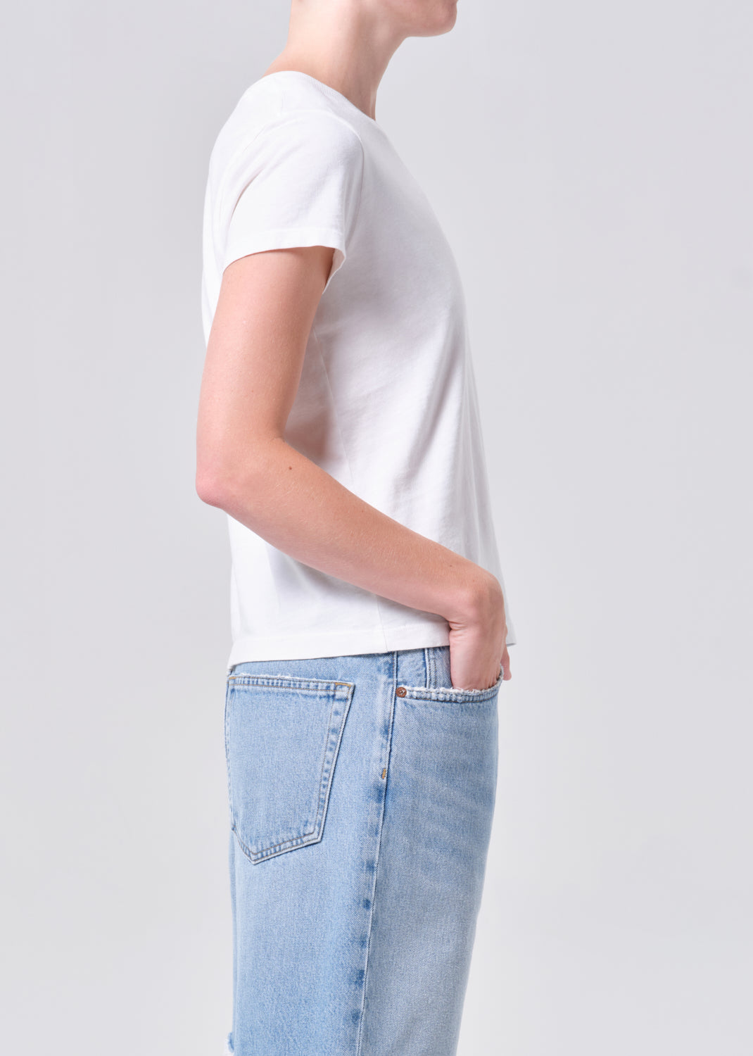 Person wearing a white t-shirt and light blue jeans on a plain background