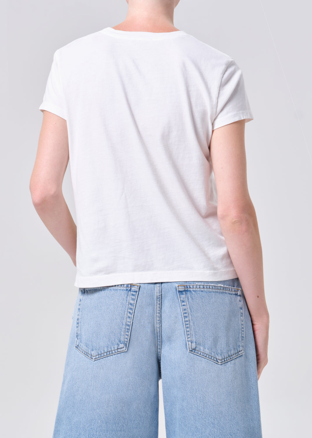 Person wearing a plain white t-shirt and light blue jeans on a gray background