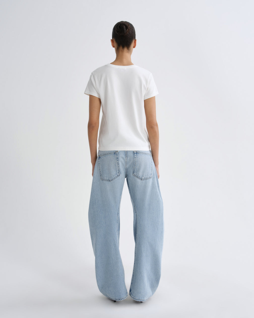 A model viewed from behind wearing a plain white short-sleeve t-shirt and light-wash wide-leg denim jeans against a light gray studio background.