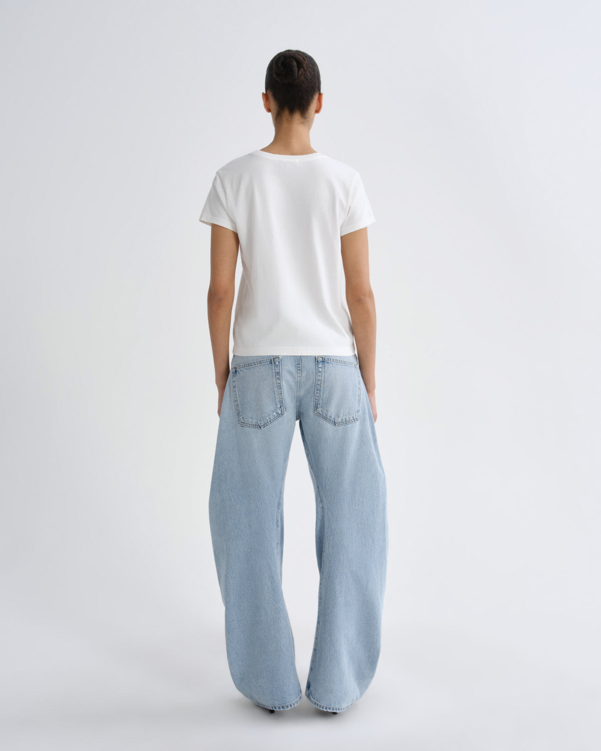 A model viewed from behind wearing a plain white short-sleeve t-shirt and light-wash wide-leg denim jeans against a light gray studio background.