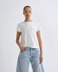 A model wearing a white short-sleeve crewneck t-shirt and light-wash blue jeans, standing against a plain light gray studio background.