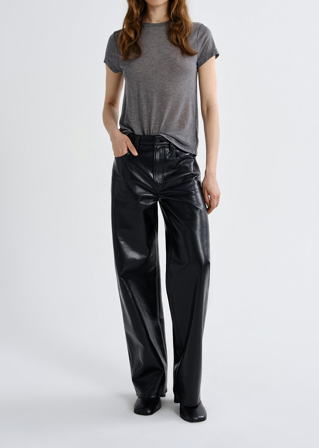 Person wearing a gray t-shirt and black shiny pants on a grey background