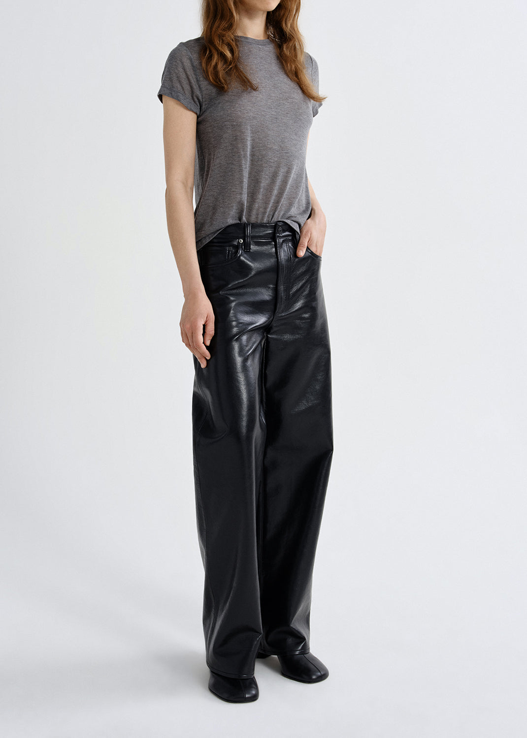 Person wearing a gray t-shirt and black leather pants on a grey background