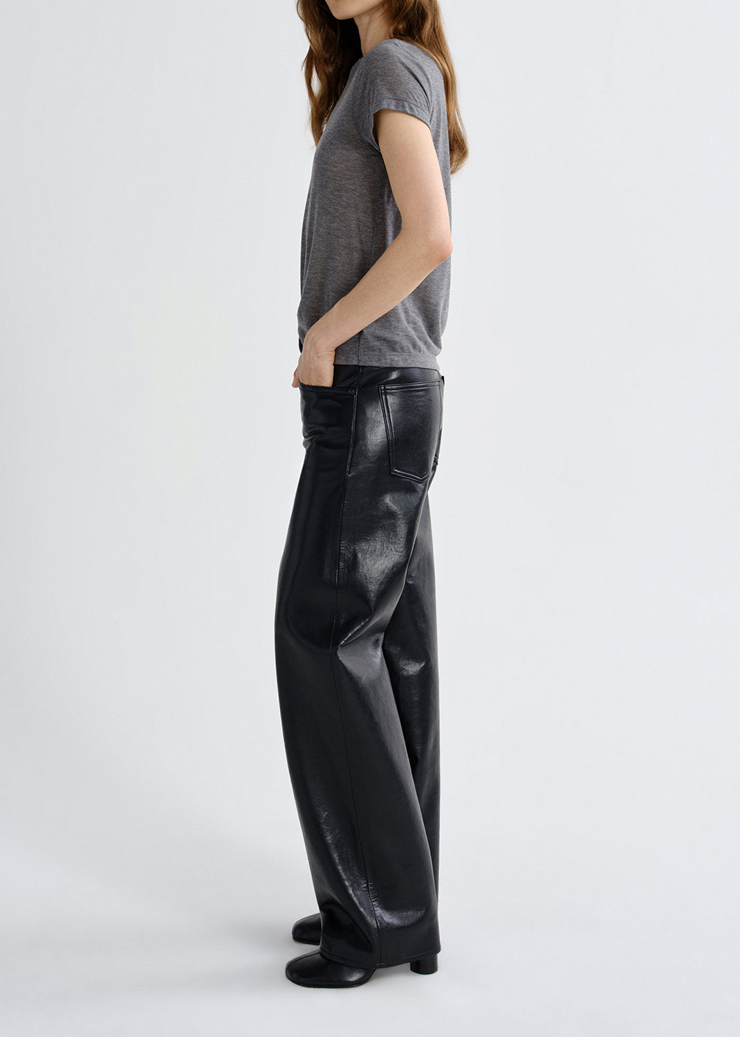 Person wearing a gray t-shirt and black leather pants on a grey background