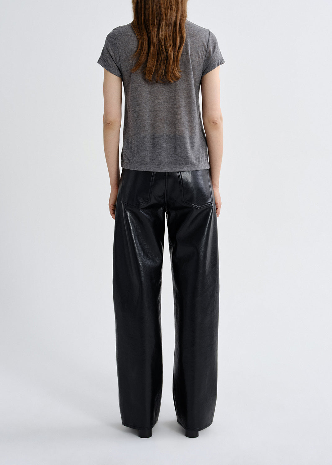 Person wearing a gray t-shirt and black leather pants on a grey background