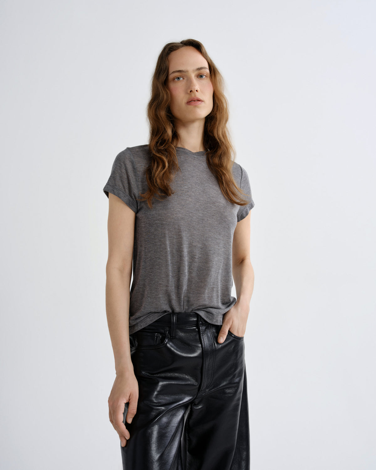 A woman modeling a short-sleeve gray t-shirt and black wide-leg faux-leather pants against a light gray studio background.