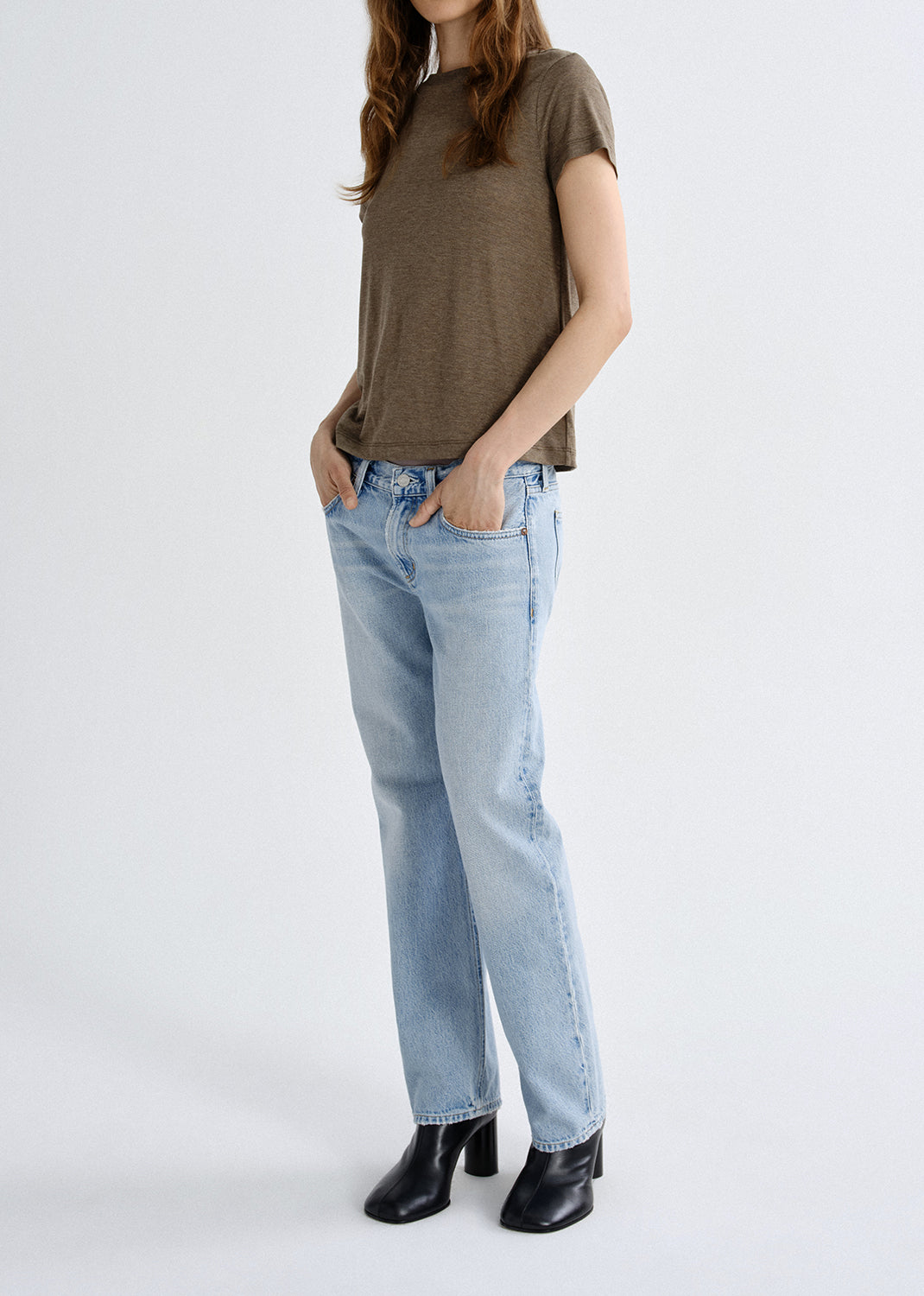 Person wearing a brown t-shirt and light blue jeans on a grey background
