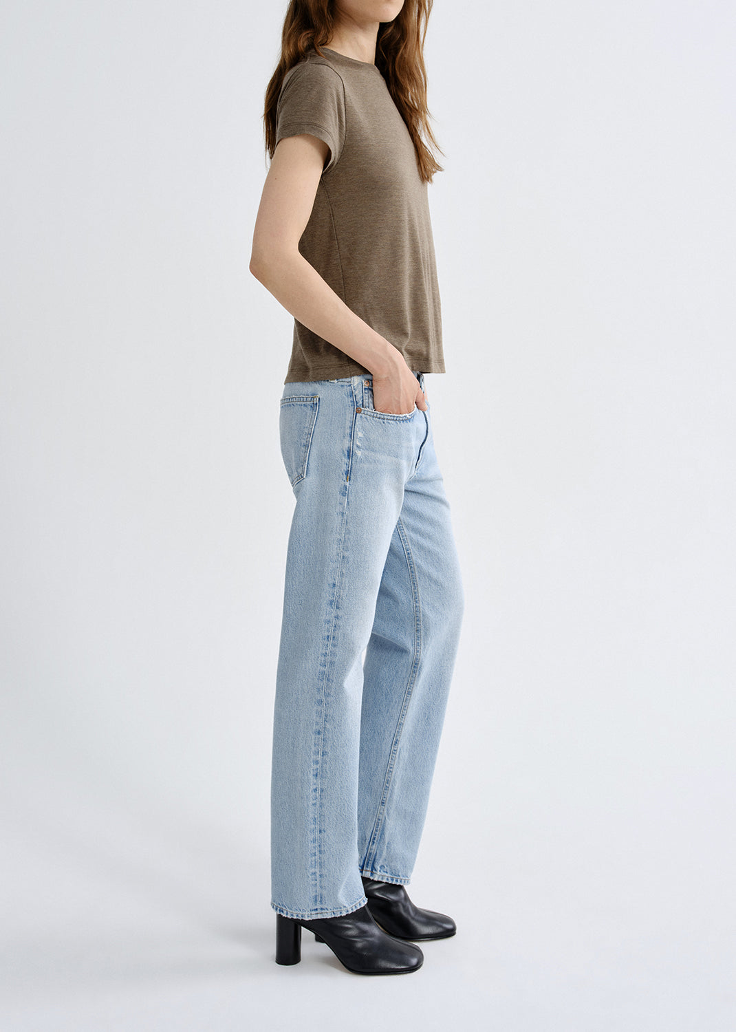 Person wearing a brown t-shirt and light blue jeans on a grey background