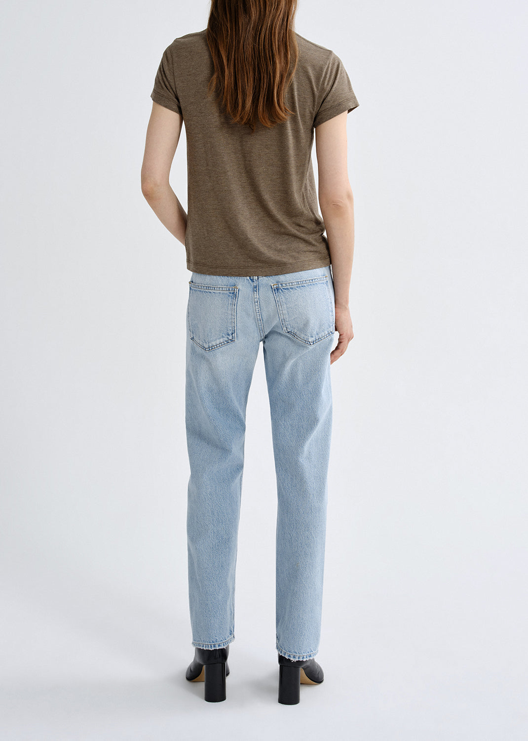 Person wearing a brown t-shirt and light blue jeans on a grey background