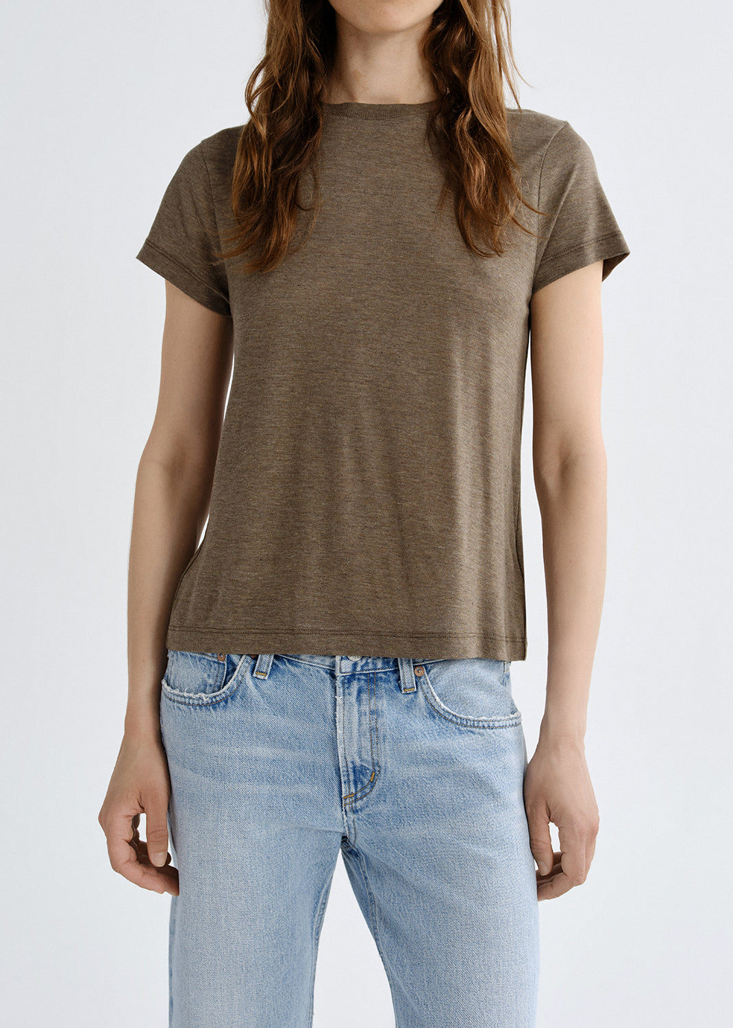 Person wearing a brown t-shirt and light blue jeans on a grey background