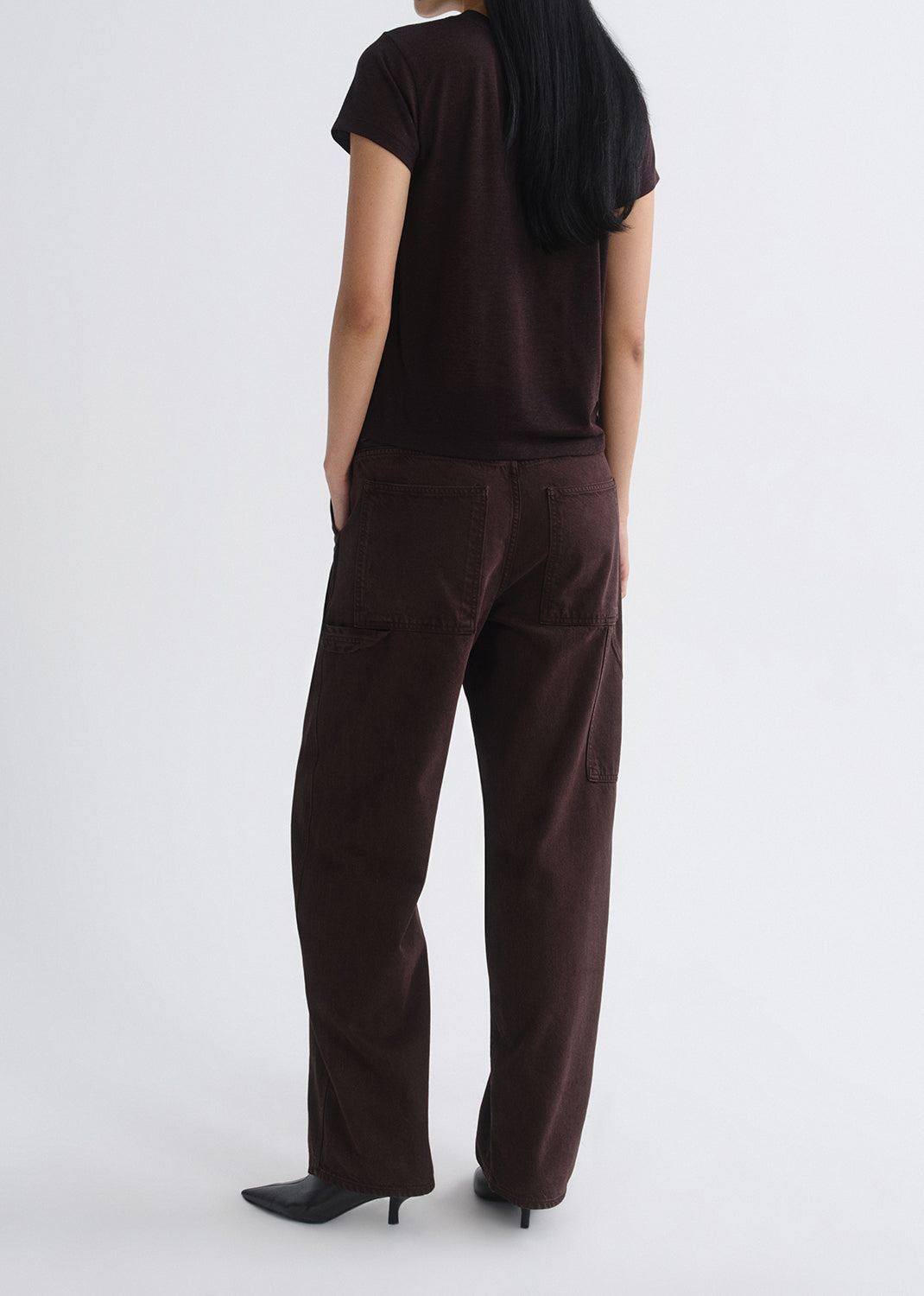 Person wearing a black shirt and brown pants on a grey background