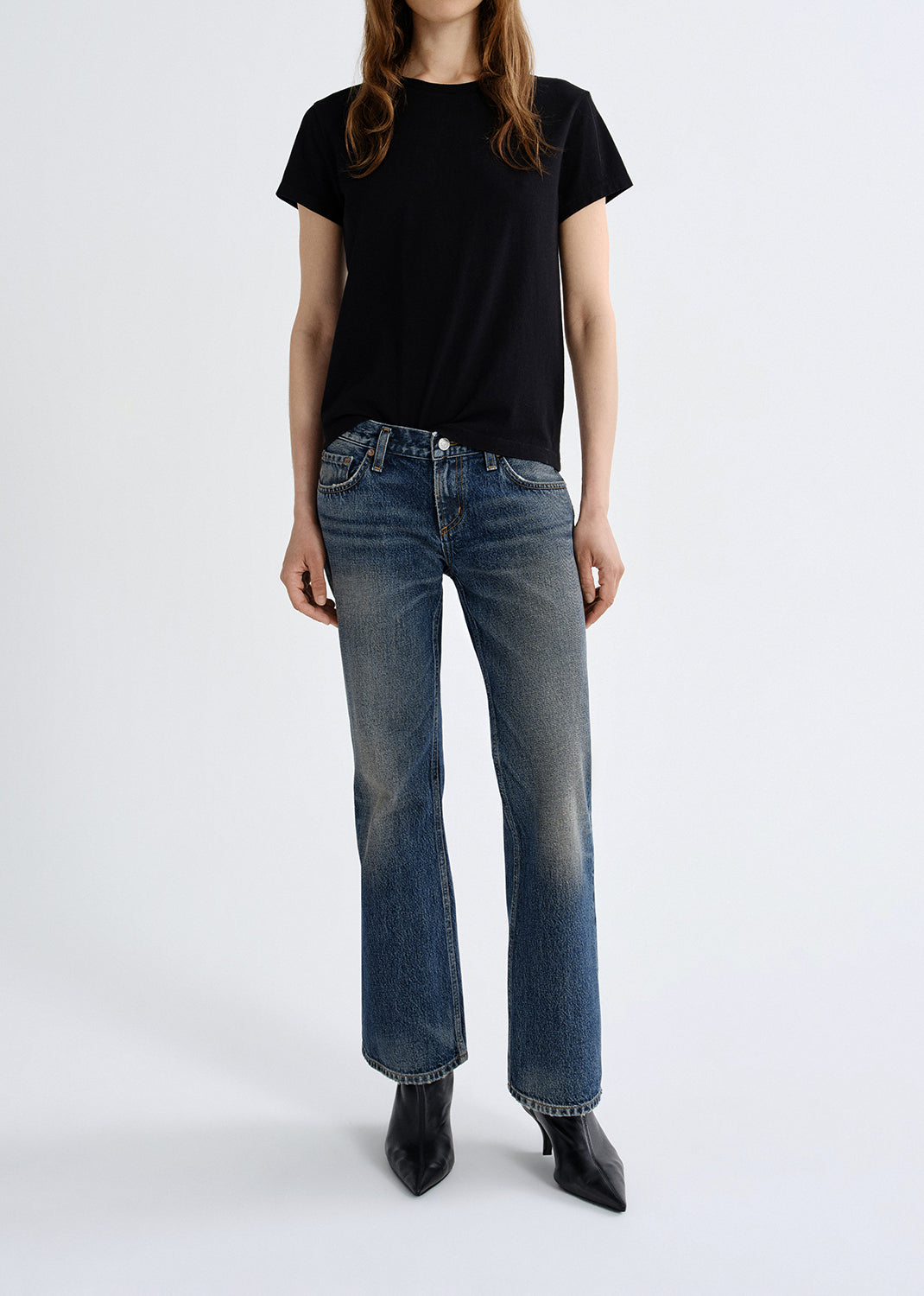 Person wearing a black t-shirt and blue jeans on a grey background