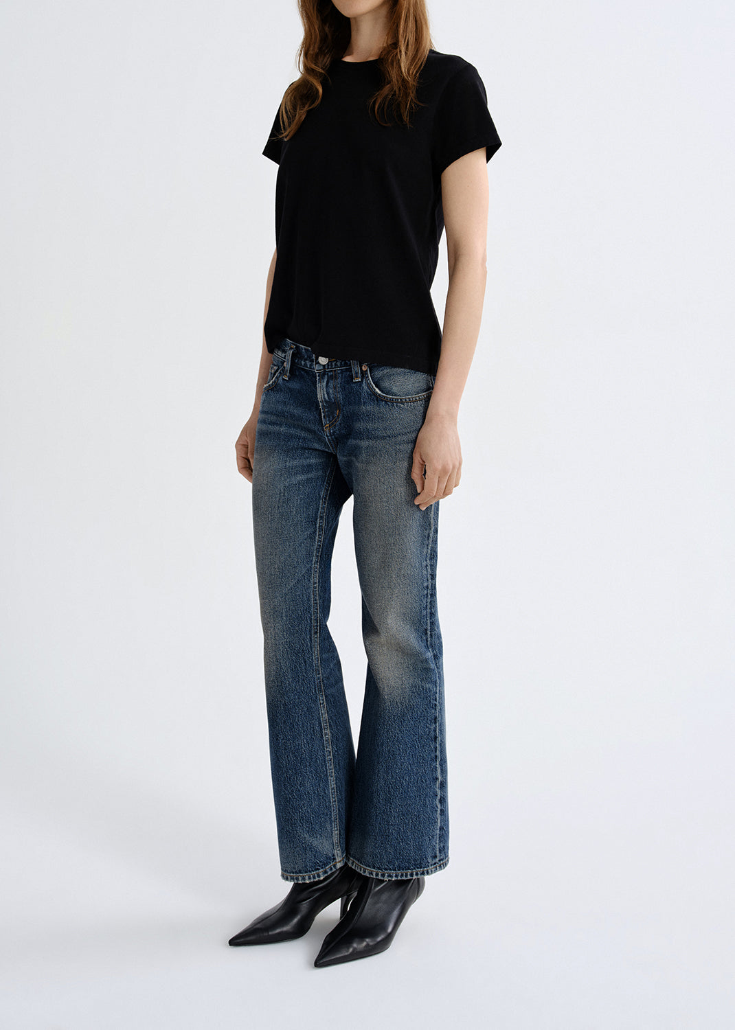 Person wearing a black t-shirt and blue jeans on a grey background