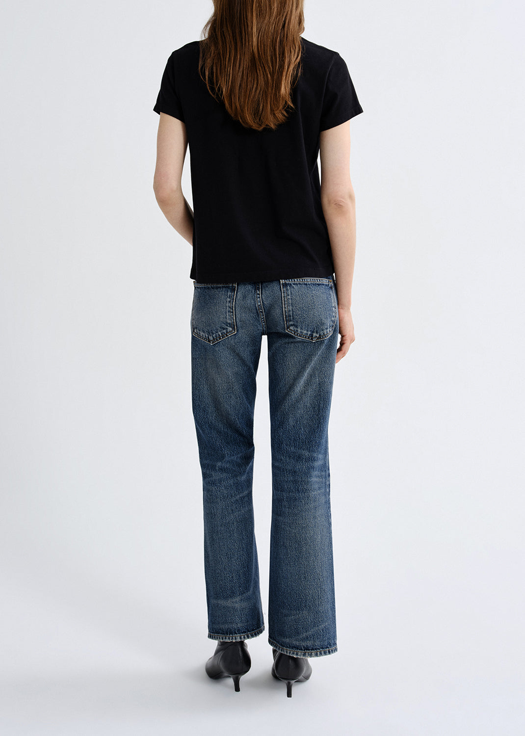 Person wearing blue jeans and a black t-shirt on a grey background