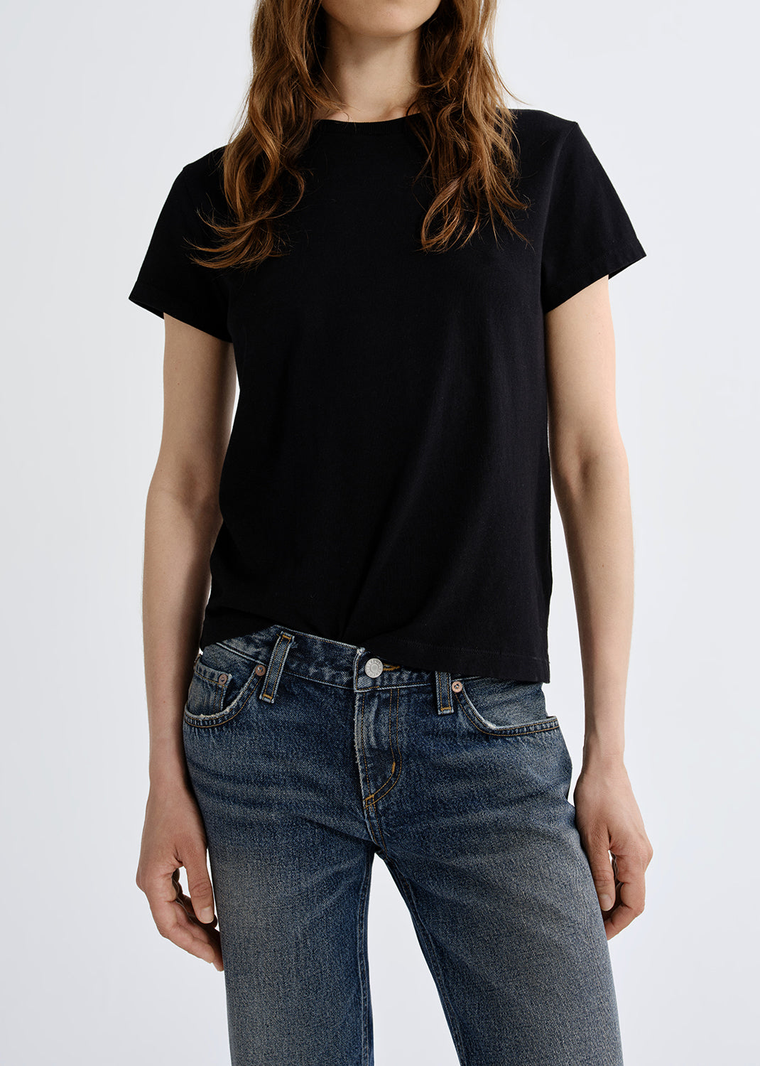 Person wearing a black t-shirt and blue jeans on a grey background