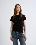 A woman modeling a black short-sleeve crewneck t-shirt paired with blue jeans, standing against a light gray studio background.