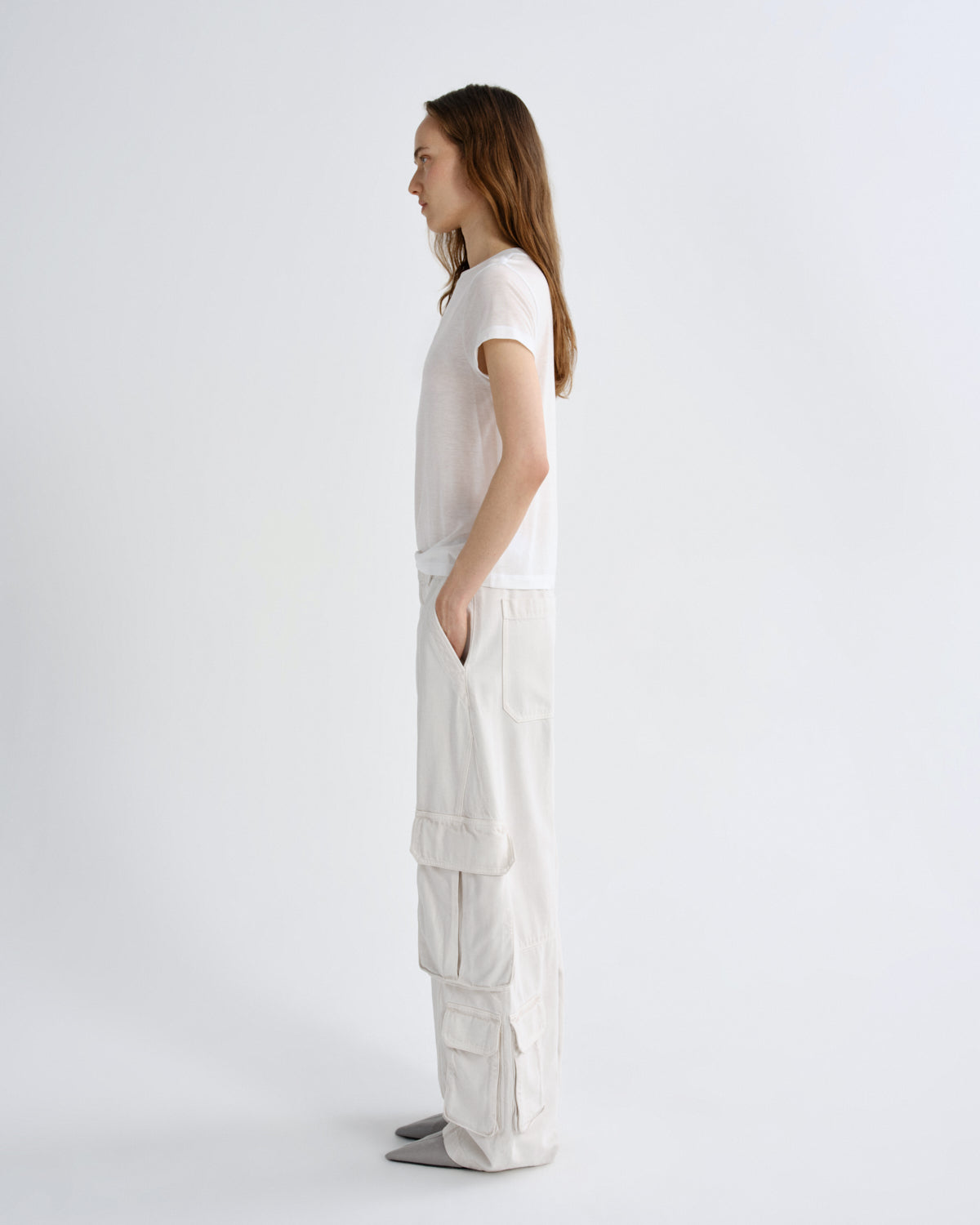 A model stands in profile wearing a white short-sleeve top and off-white wide-leg cargo pants against a plain light gray studio background.