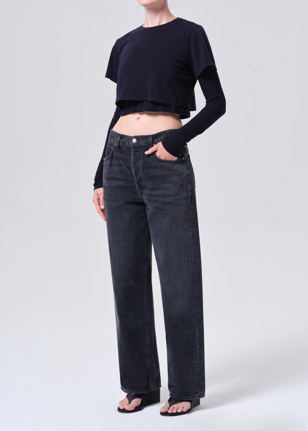 Person wearing a black cropped top and dark jeans on a white background