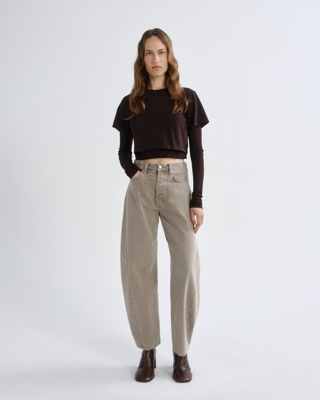 Woman wearing a brown sweater and beige pants on a white background